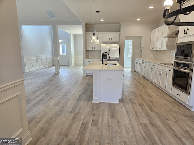 kitchen with white cabinetry, an island with sink, stainless steel appliances, pendant lighting, and sink