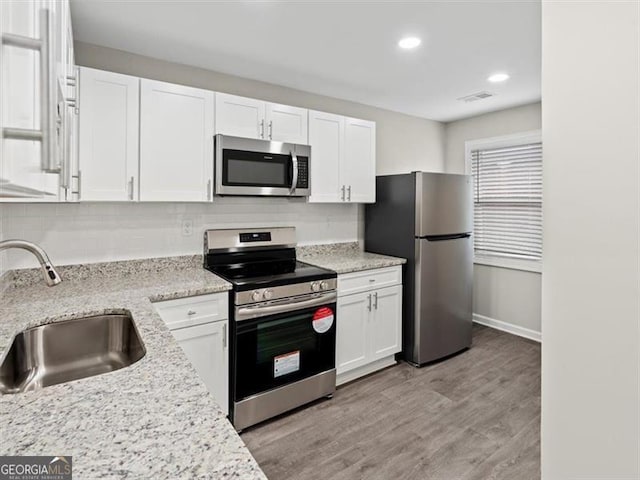 kitchen featuring light hardwood / wood-style floors, sink, white cabinetry, appliances with stainless steel finishes, and light stone countertops