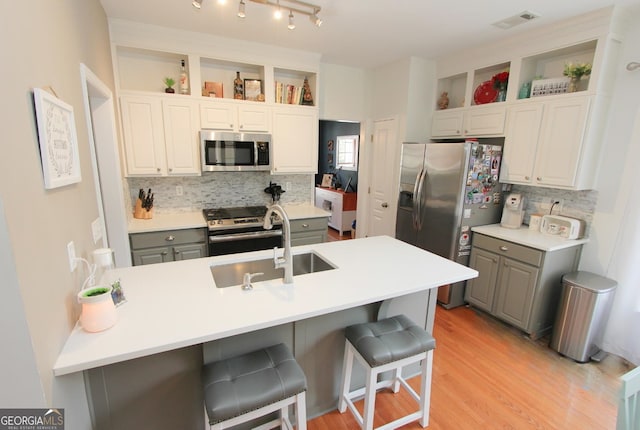 kitchen featuring gray cabinetry, backsplash, appliances with stainless steel finishes, and a breakfast bar area