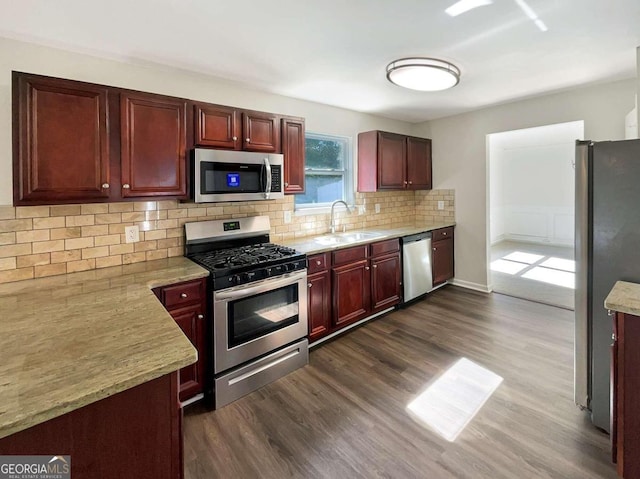 kitchen featuring appliances with stainless steel finishes, dark wood-type flooring, light stone counters, tasteful backsplash, and sink