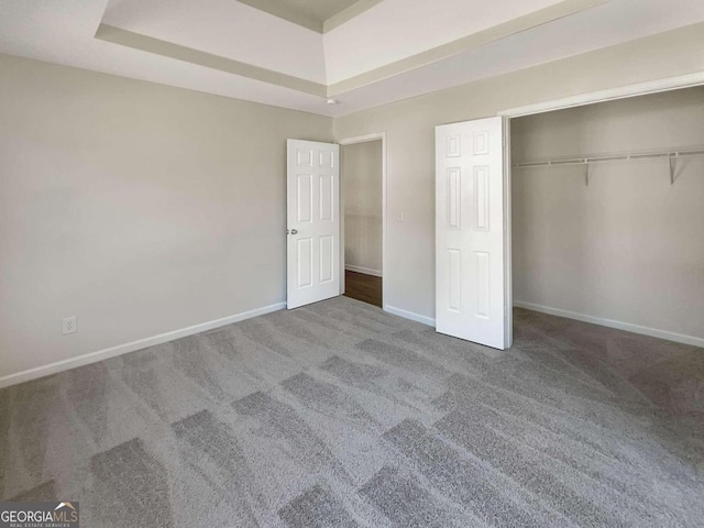 unfurnished bedroom featuring carpet, a raised ceiling, and a closet