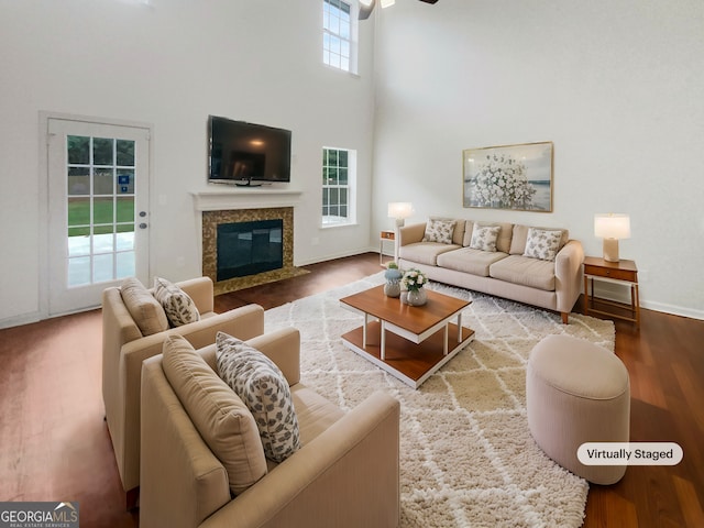 living room with a high ceiling, a premium fireplace, hardwood / wood-style flooring, and a healthy amount of sunlight