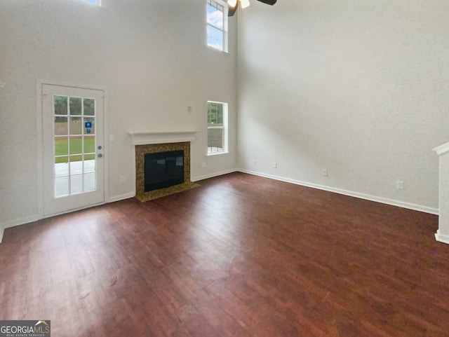 unfurnished living room with ceiling fan, a fireplace, dark wood-type flooring, and a high ceiling