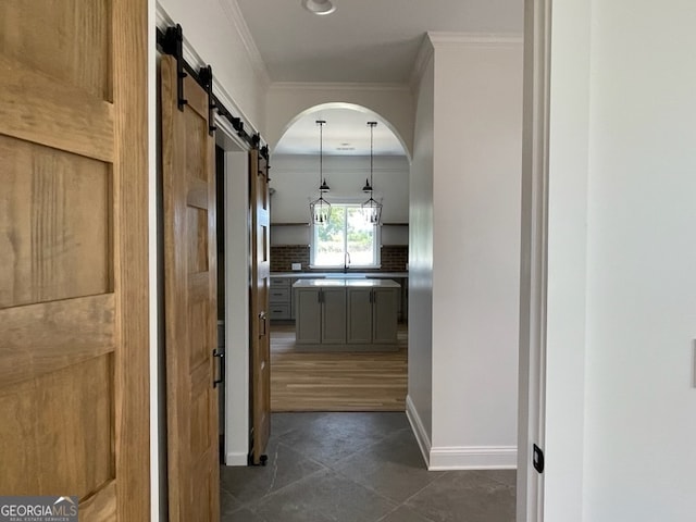 hall with ornamental molding, sink, dark tile patterned flooring, and a barn door