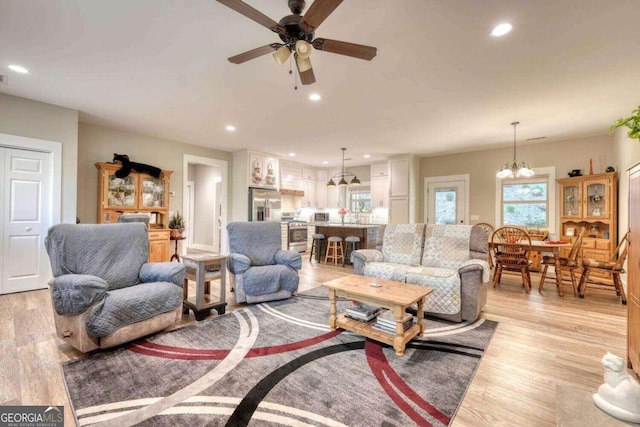 living room with ceiling fan with notable chandelier and light wood-type flooring