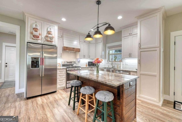 kitchen featuring pendant lighting, custom exhaust hood, white cabinetry, appliances with stainless steel finishes, and a center island