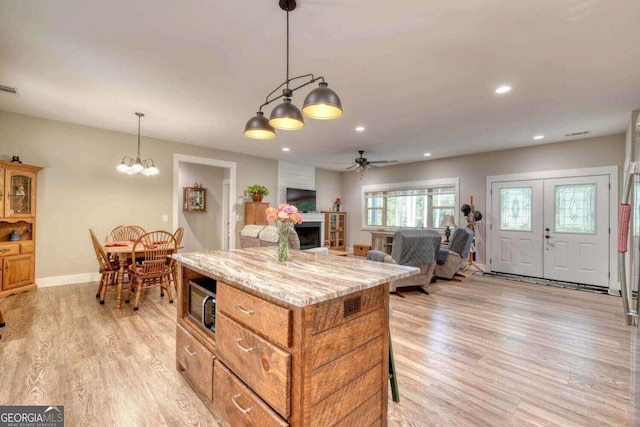 kitchen with pendant lighting, light hardwood / wood-style floors, a center island, ceiling fan with notable chandelier, and light stone countertops