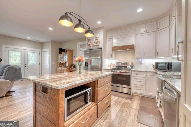 kitchen featuring light stone counters, a center island, white cabinetry, hanging light fixtures, and appliances with stainless steel finishes