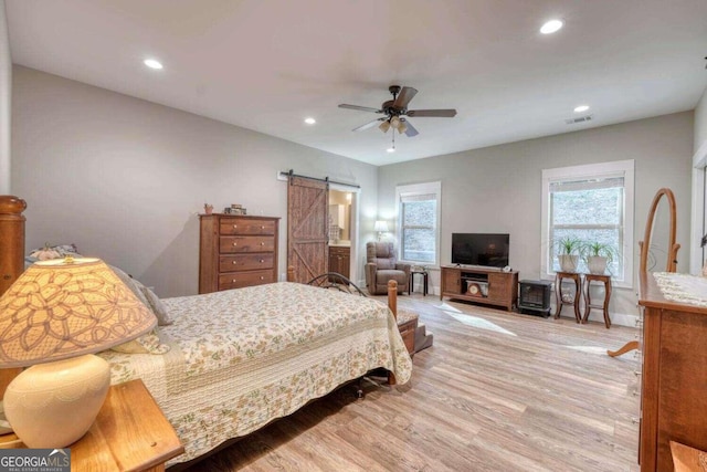 bedroom with ceiling fan, light wood-type flooring, a barn door, and multiple windows