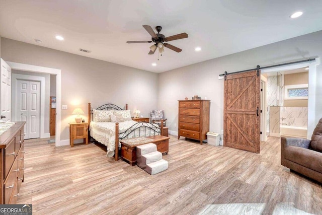 bedroom with light wood-type flooring, ceiling fan, ensuite bathroom, and a barn door