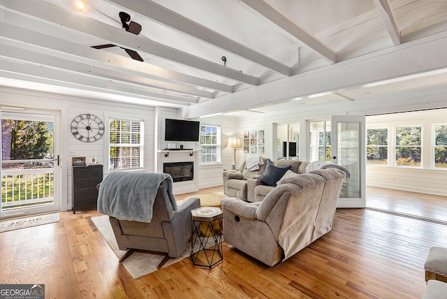 living room with beamed ceiling, wood walls, ceiling fan, and light hardwood / wood-style flooring