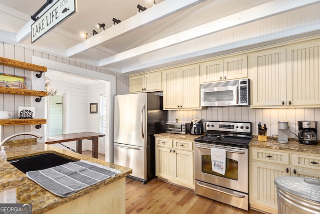 kitchen with vaulted ceiling with beams, sink, cream cabinets, light hardwood / wood-style flooring, and stainless steel appliances