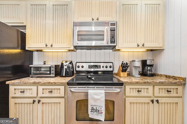 kitchen with light stone countertops, stainless steel appliances, and cream cabinetry