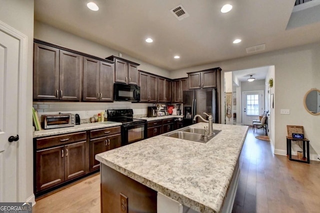 kitchen featuring sink, dark brown cabinets, a kitchen island with sink, black appliances, and light wood-type flooring