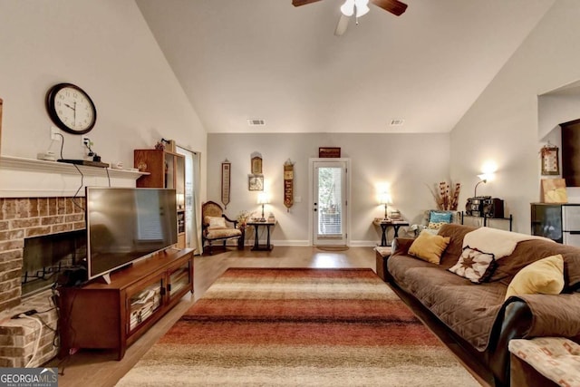 living room with a brick fireplace, vaulted ceiling, light hardwood / wood-style floors, and ceiling fan