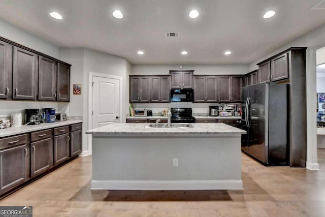 kitchen featuring an island with sink, black appliances, dark brown cabinetry, and sink