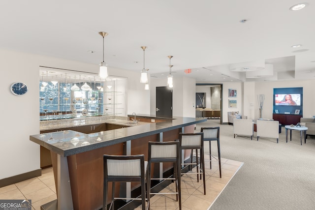 kitchen featuring a large island with sink, a breakfast bar, decorative light fixtures, and light colored carpet