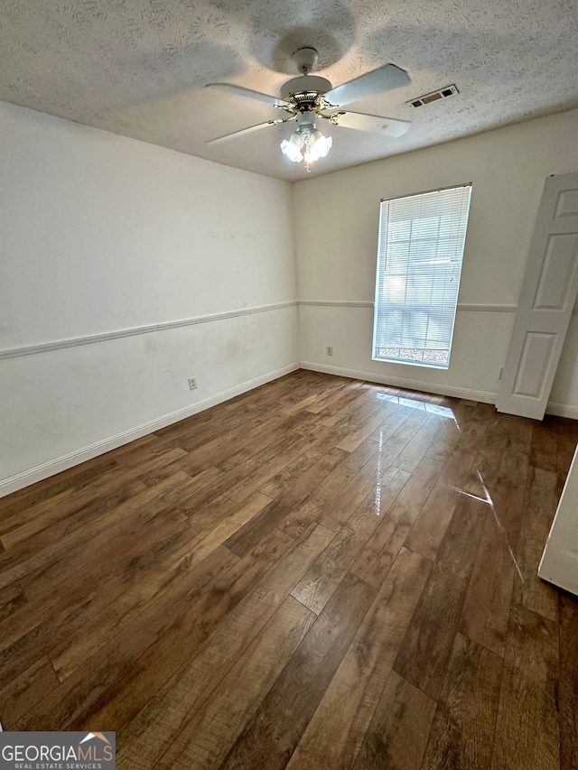 spare room featuring dark wood-type flooring, ceiling fan, and a textured ceiling