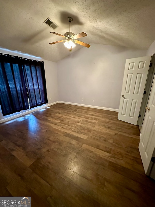 empty room featuring dark hardwood / wood-style flooring, lofted ceiling, a textured ceiling, and ceiling fan