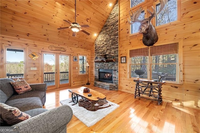 living room with ceiling fan, wooden walls, wood-type flooring, high vaulted ceiling, and a fireplace