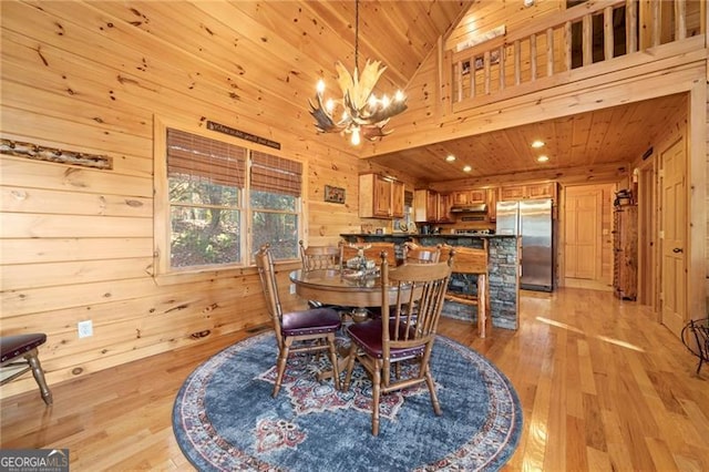 dining space featuring high vaulted ceiling, wood walls, a chandelier, light hardwood / wood-style floors, and wood ceiling