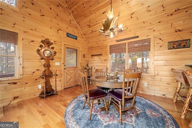 dining space featuring wood walls, light hardwood / wood-style floors, high vaulted ceiling, and a chandelier