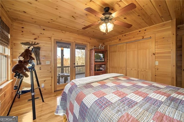 bedroom with access to exterior, light hardwood / wood-style floors, a closet, and wooden walls