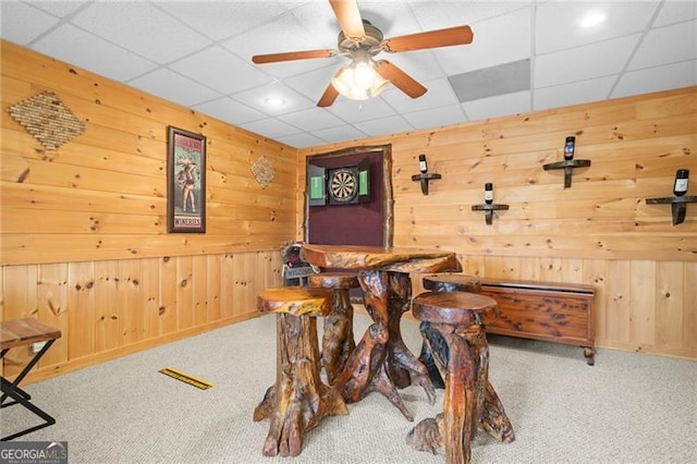 dining space featuring carpet flooring, a drop ceiling, and wood walls