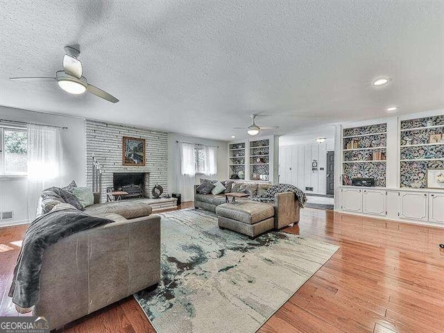 living room featuring a textured ceiling, light hardwood / wood-style floors, a fireplace, and built in shelves