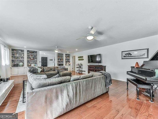 living room with built in shelves, light wood-type flooring, and ceiling fan