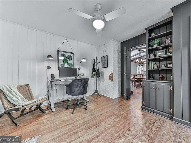 office area with light wood-type flooring, wood walls, and ceiling fan