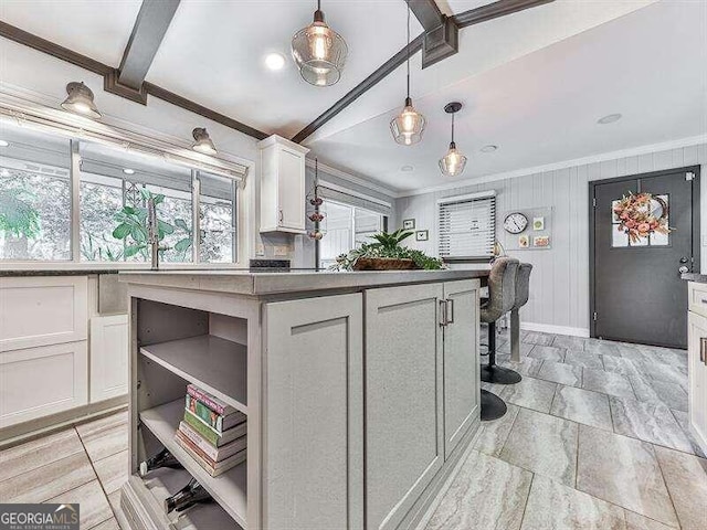 kitchen with hanging light fixtures, white cabinets, a kitchen island, beam ceiling, and ornamental molding