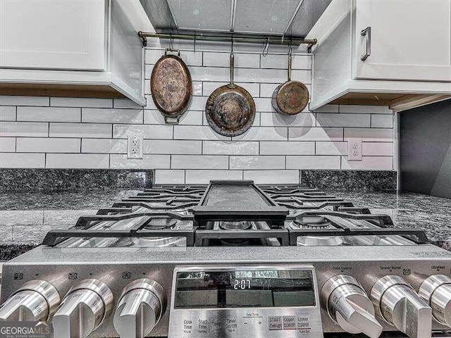 interior details featuring dark stone counters, decorative backsplash, stainless steel range with gas cooktop, and white cabinets