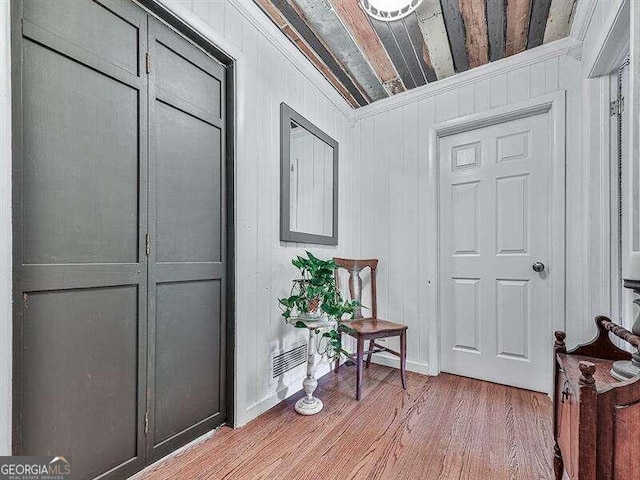 hall featuring wooden walls, light hardwood / wood-style flooring, and ornamental molding