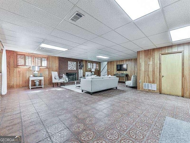 unfurnished living room with a brick fireplace, wooden walls, and a paneled ceiling