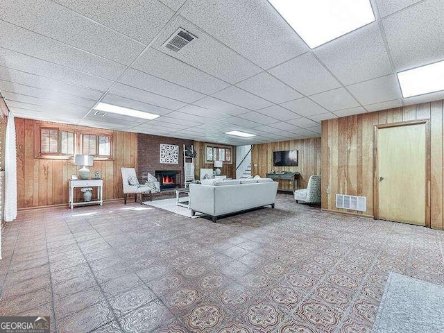 unfurnished living room featuring a drop ceiling and wooden walls