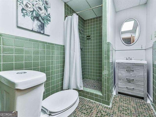 bathroom with vanity, a drop ceiling, walk in shower, tile walls, and toilet