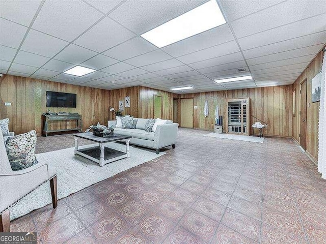 unfurnished living room with a drop ceiling and wood walls