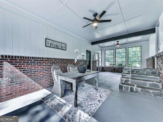 living room with concrete floors, brick wall, beamed ceiling, and ceiling fan