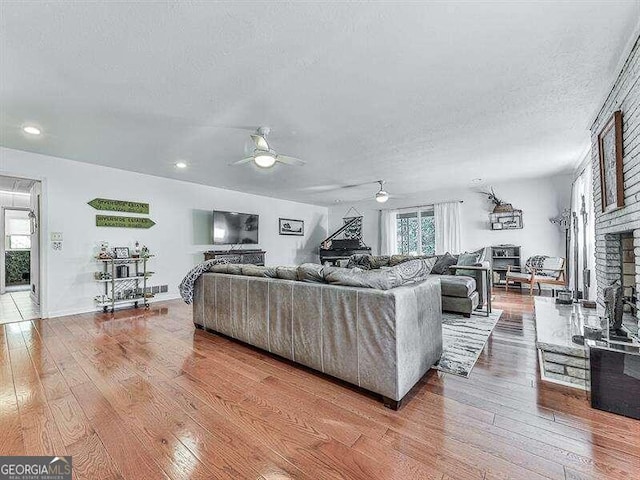 living room featuring light wood-type flooring, a textured ceiling, and ceiling fan