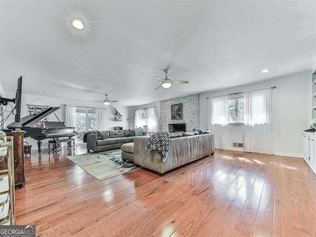 living room featuring light hardwood / wood-style flooring, ceiling fan, plenty of natural light, and a fireplace