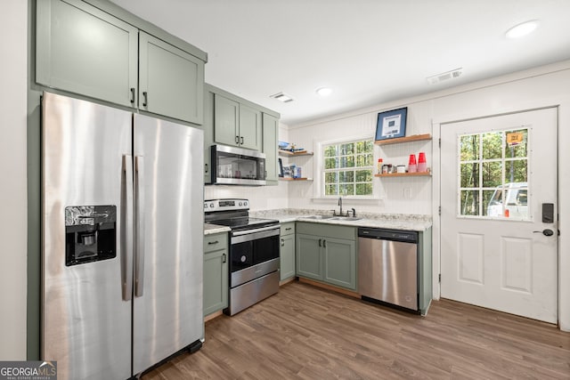 kitchen with appliances with stainless steel finishes, green cabinetry, dark hardwood / wood-style flooring, and sink