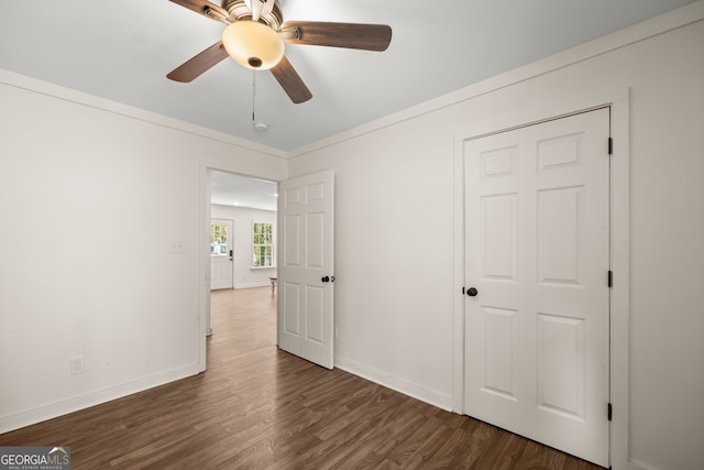 unfurnished bedroom featuring ornamental molding, dark wood-type flooring, ceiling fan, and a closet