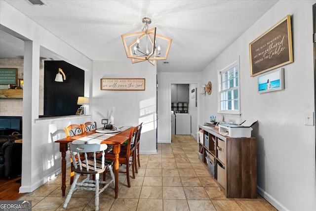 dining area featuring a textured ceiling, washer and clothes dryer, a chandelier, and a brick fireplace