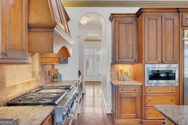 kitchen with premium range hood, arched walkways, stainless steel range, crown molding, and brown cabinets
