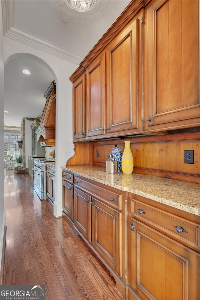 kitchen with wood walls, wood-type flooring, high end stainless steel range, light stone counters, and ornamental molding