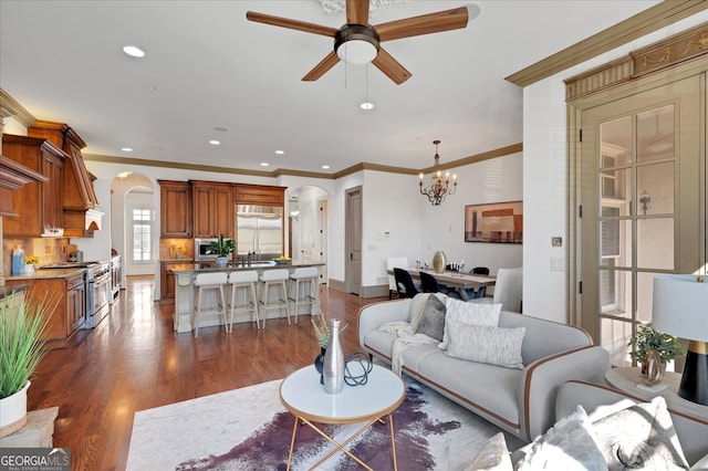 living room with ceiling fan with notable chandelier, ornamental molding, dark hardwood / wood-style flooring, and sink