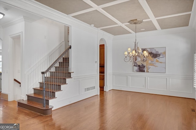 stairs with ornamental molding, coffered ceiling, an inviting chandelier, and wood-type flooring