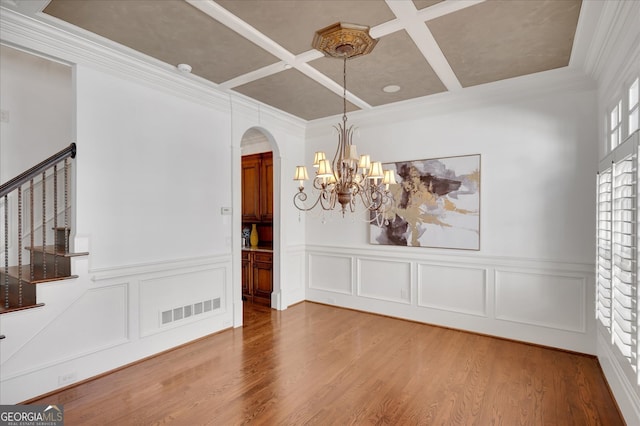 spare room with ornamental molding, hardwood / wood-style floors, coffered ceiling, and an inviting chandelier