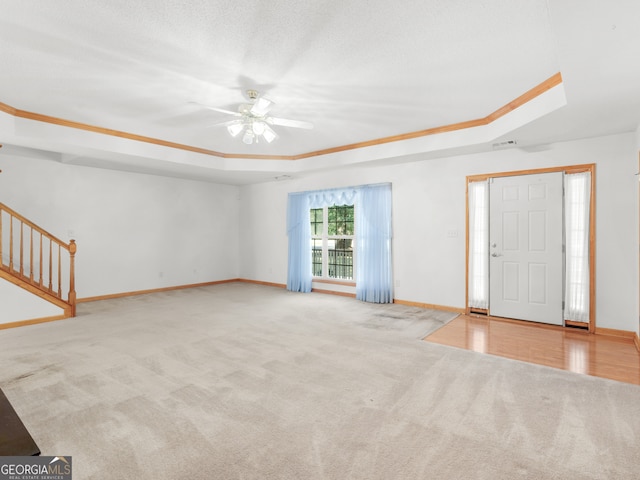 interior space featuring crown molding, a tray ceiling, light colored carpet, and ceiling fan